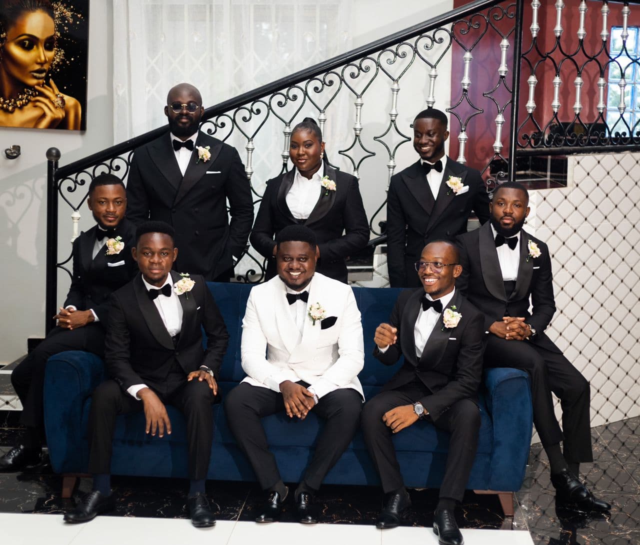 A group in black and white tuxedos posing on a blue sofa by a staircase.