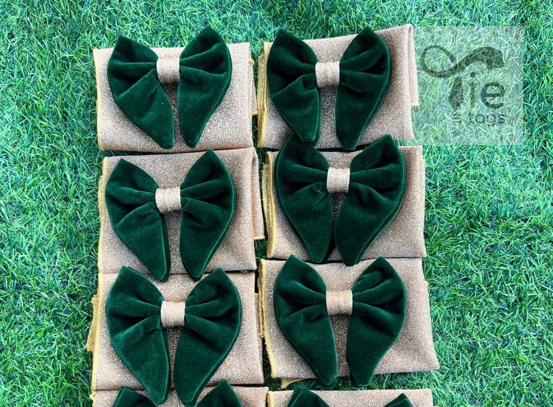 Dark green velvet bow ties on gold shimmering fabric squares arranged on green grass.