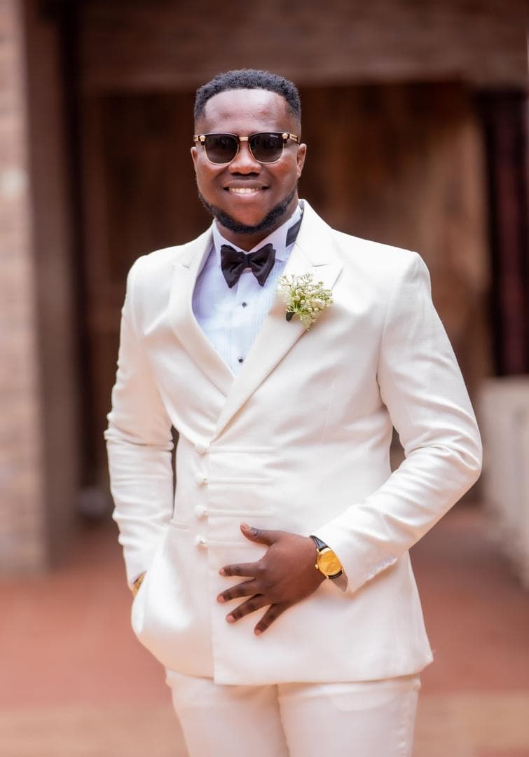 Smiling man in a white tuxedo, black bow tie, and sunglasses with a white boutonniere.