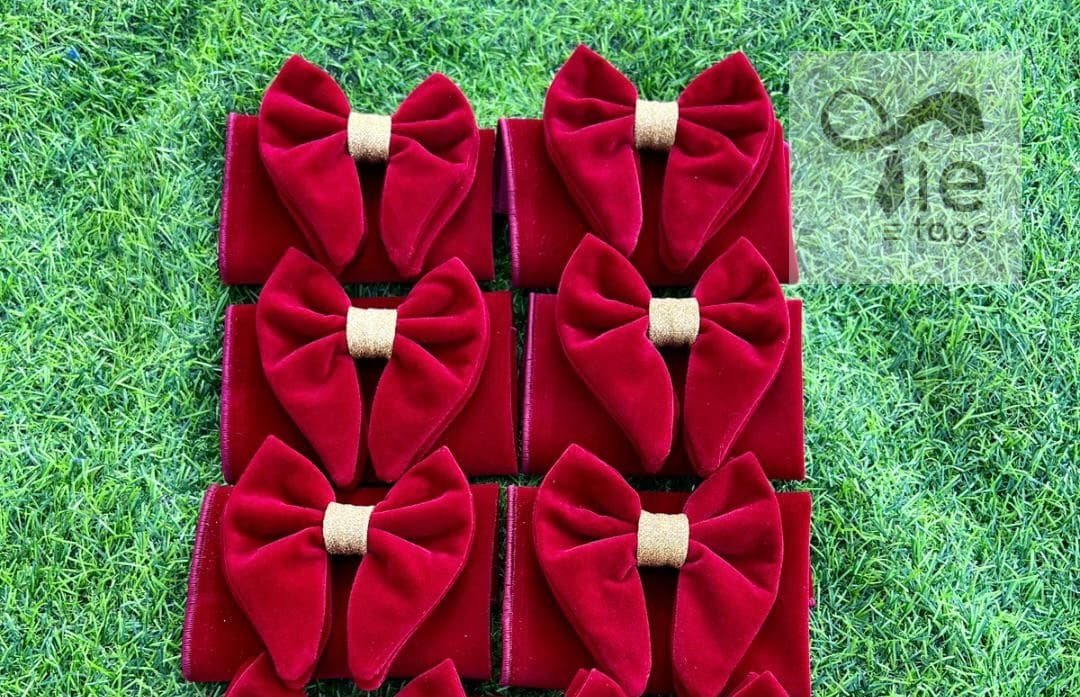 Six deep red velvet bows with gold glitter centers arranged on green artificial grass.