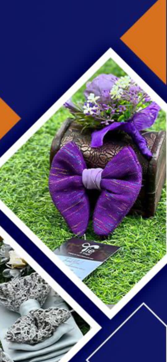 Purple textured bow tie and floral boutonniere resting on a small chest over green grass.