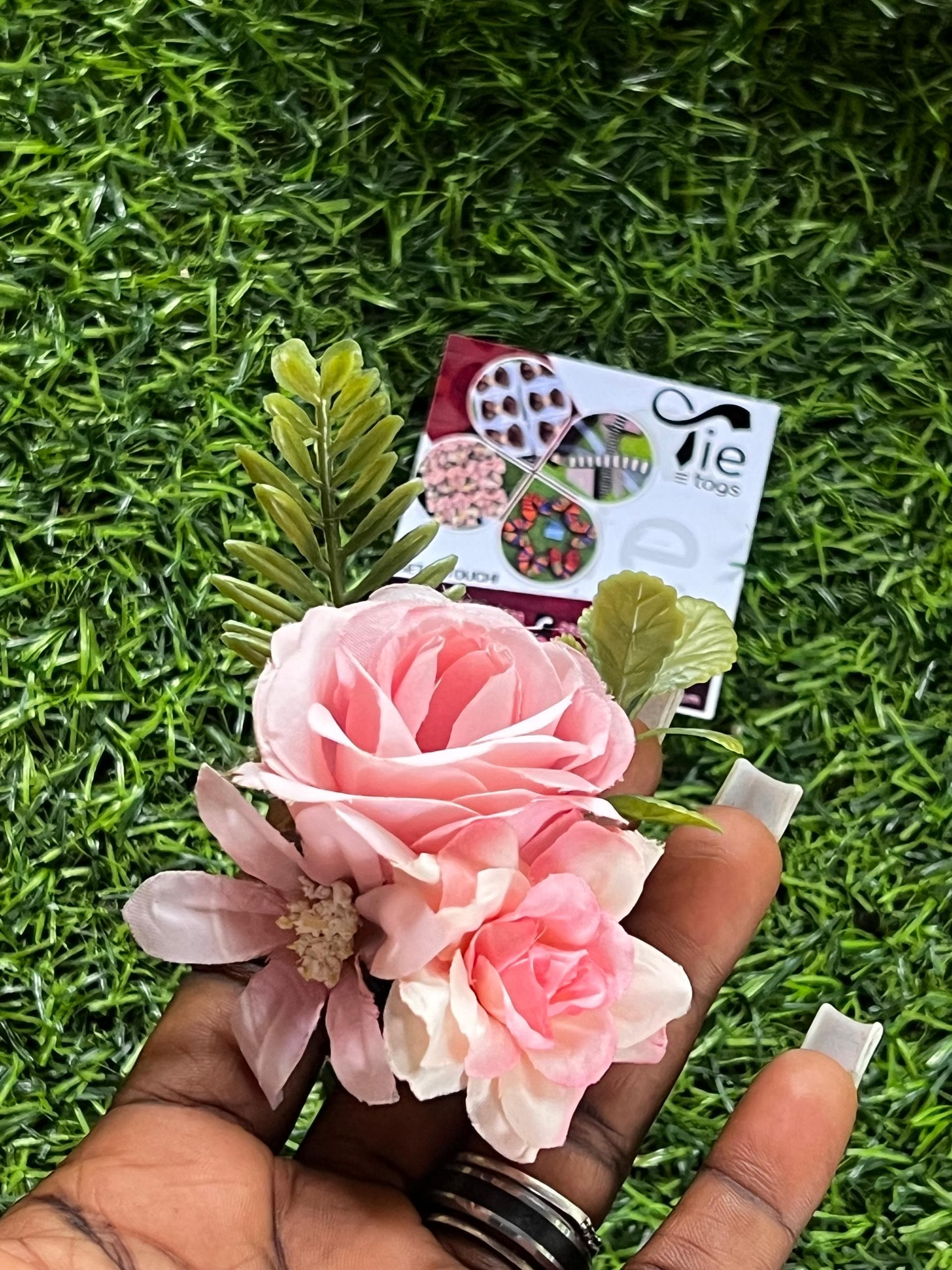 Hand holding a pink rose and daisy floral arrangement over a background of green grass.