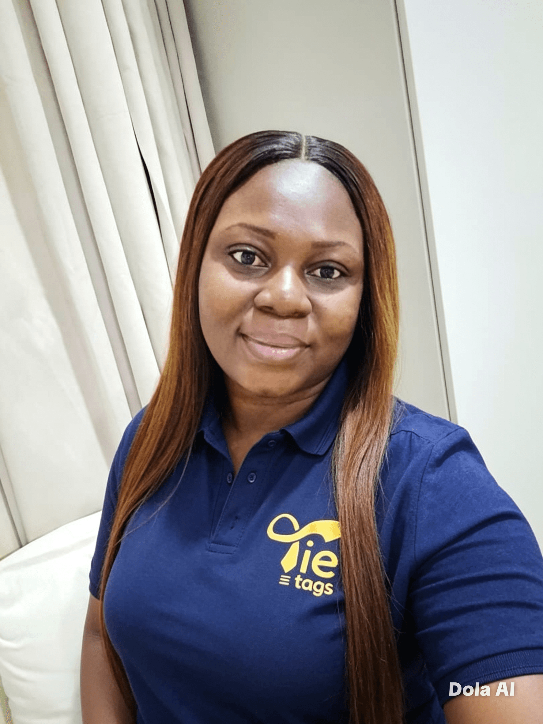 Smiling woman with long brown hair wearing a navy blue Tie tags polo shirt.