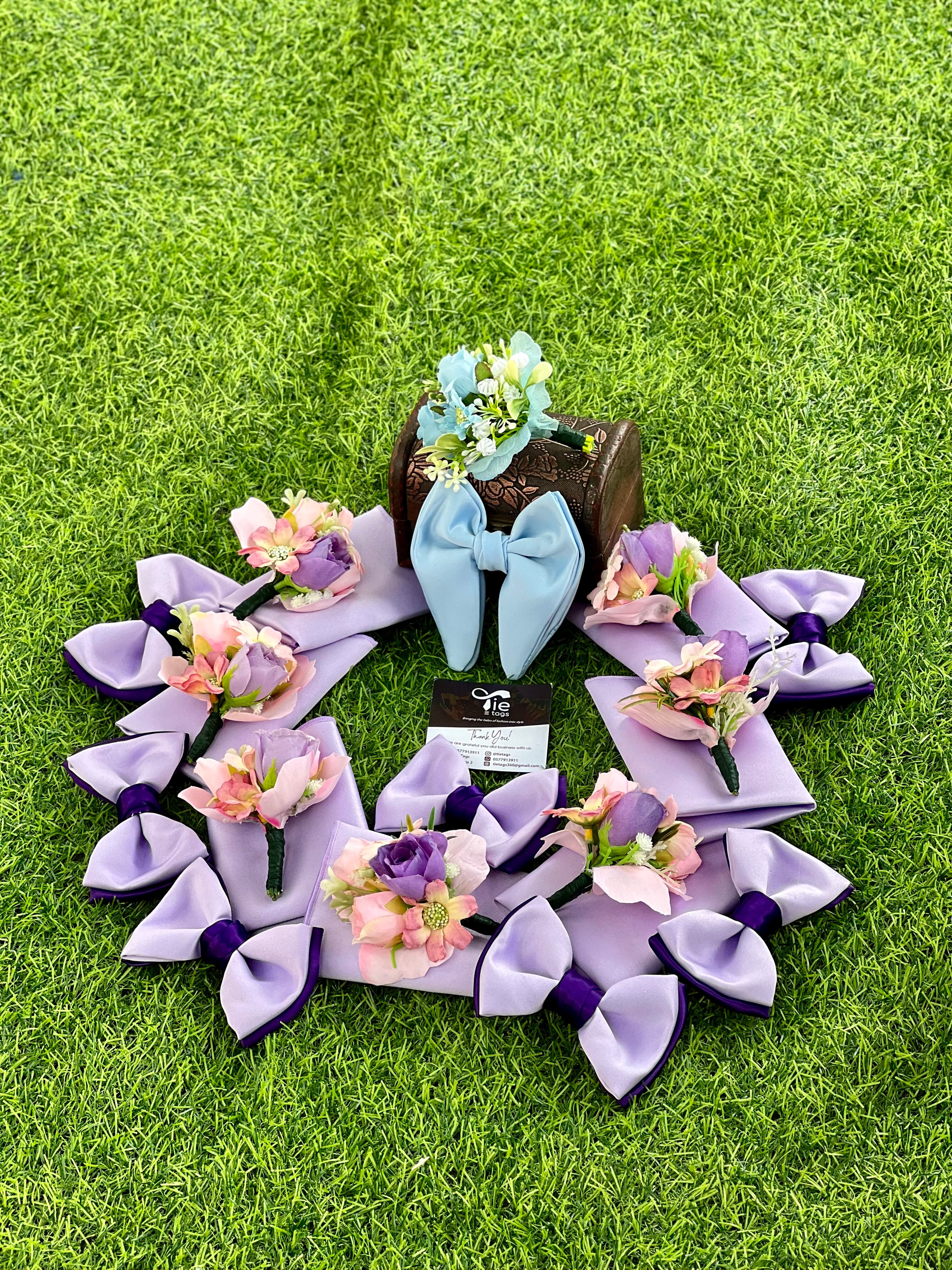 Circular arrangement of purple and blue bow ties and floral boutonnieres on green grass.