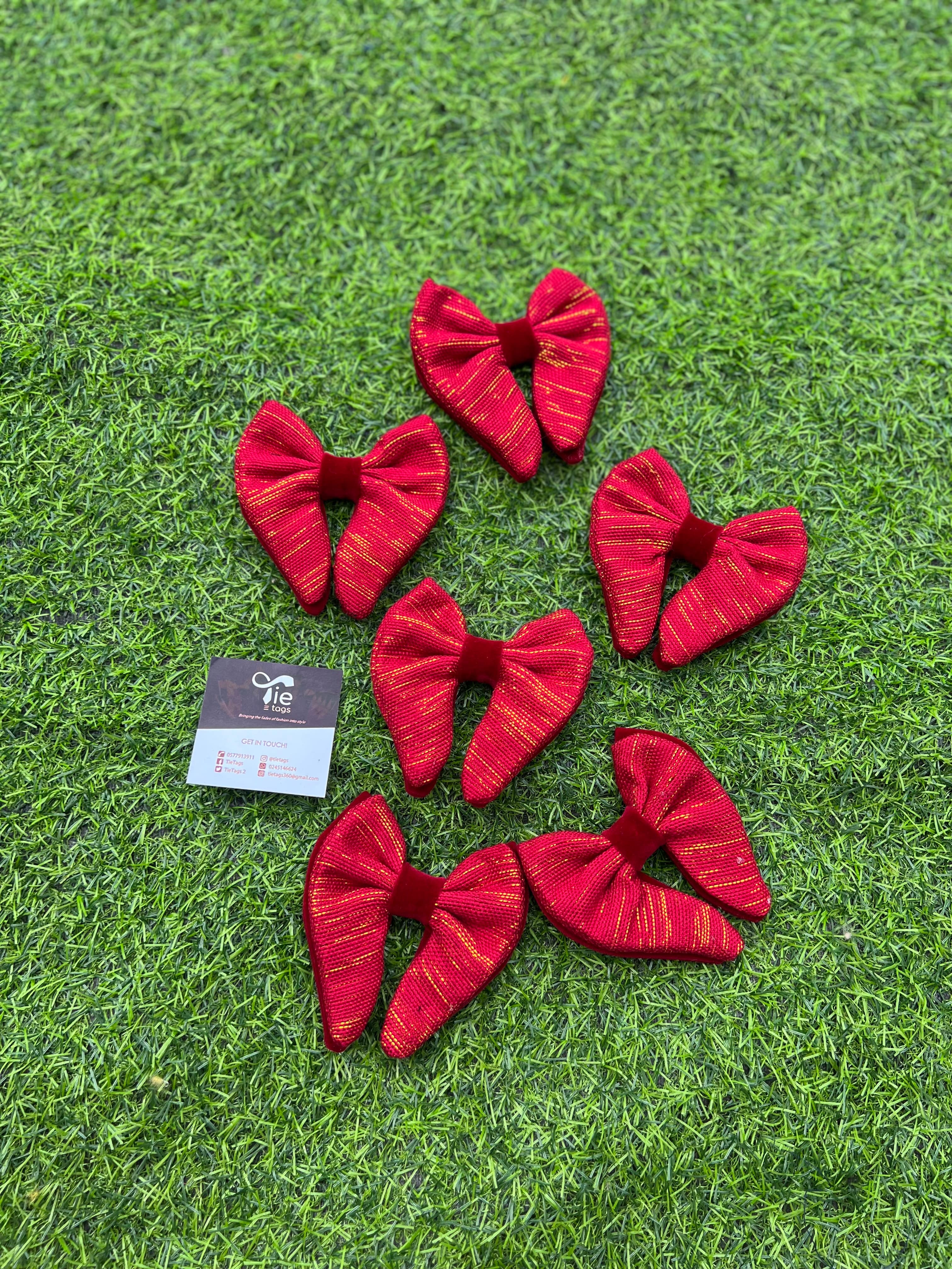 Six red and gold pinstriped bow ties on green artificial grass with a business card.