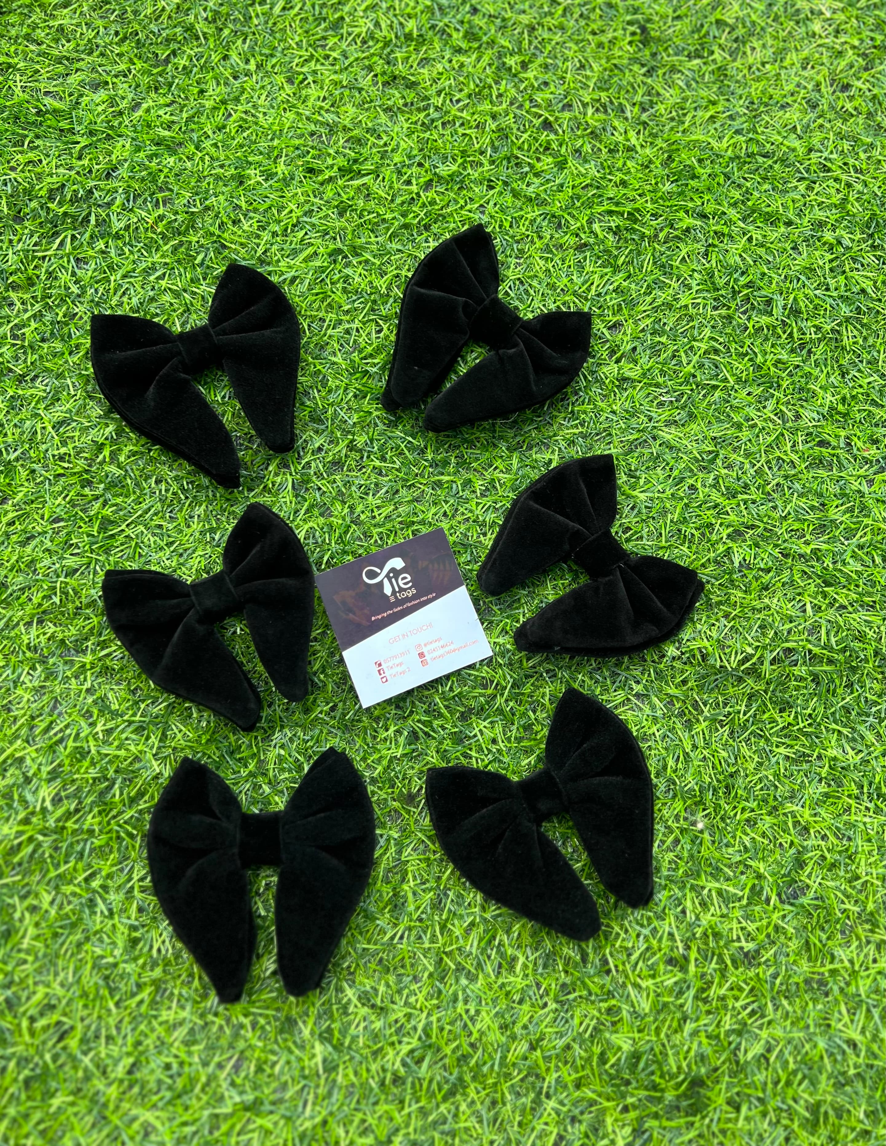 Six black velvet bows surrounding a business card on a green artificial grass background.