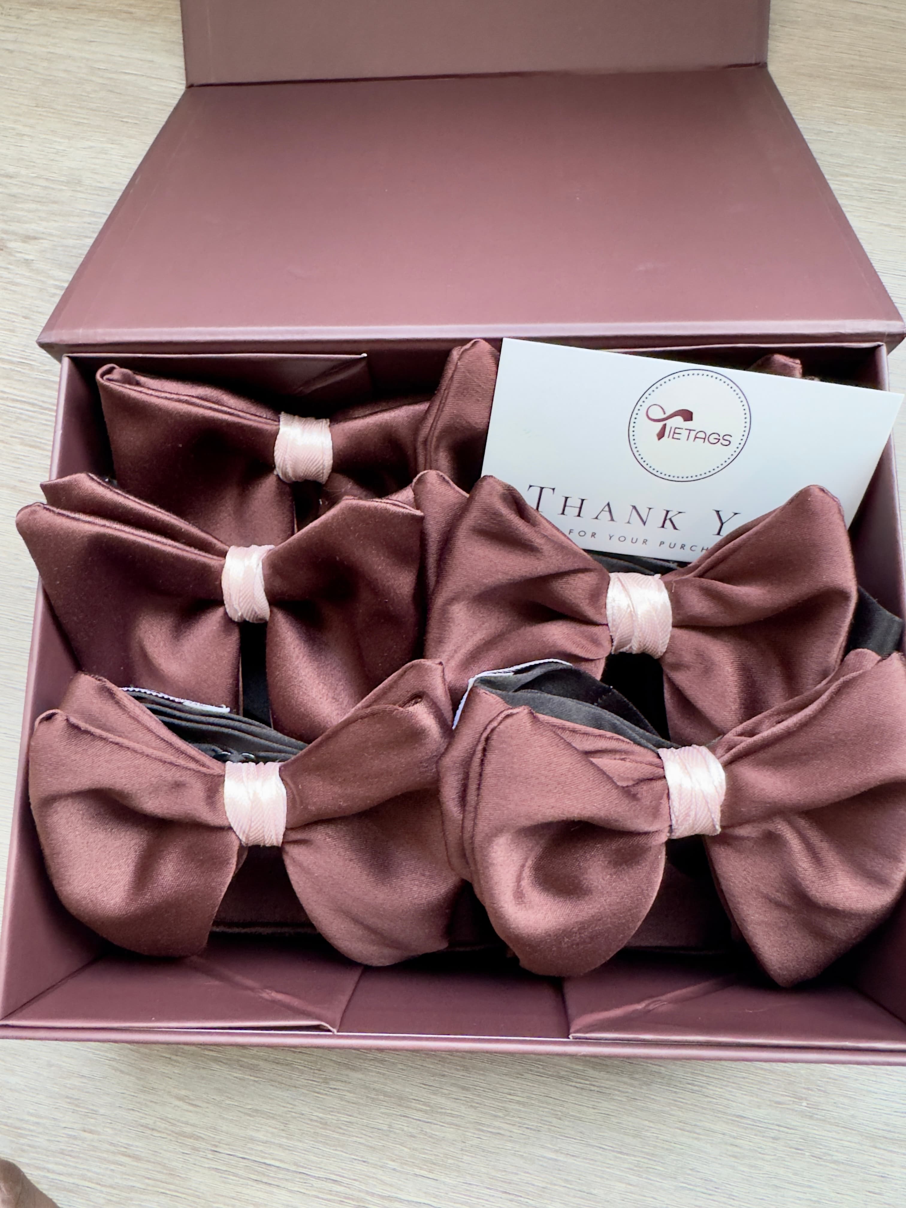 Brown satin bow ties with pink centers in a maroon gift box with a card.