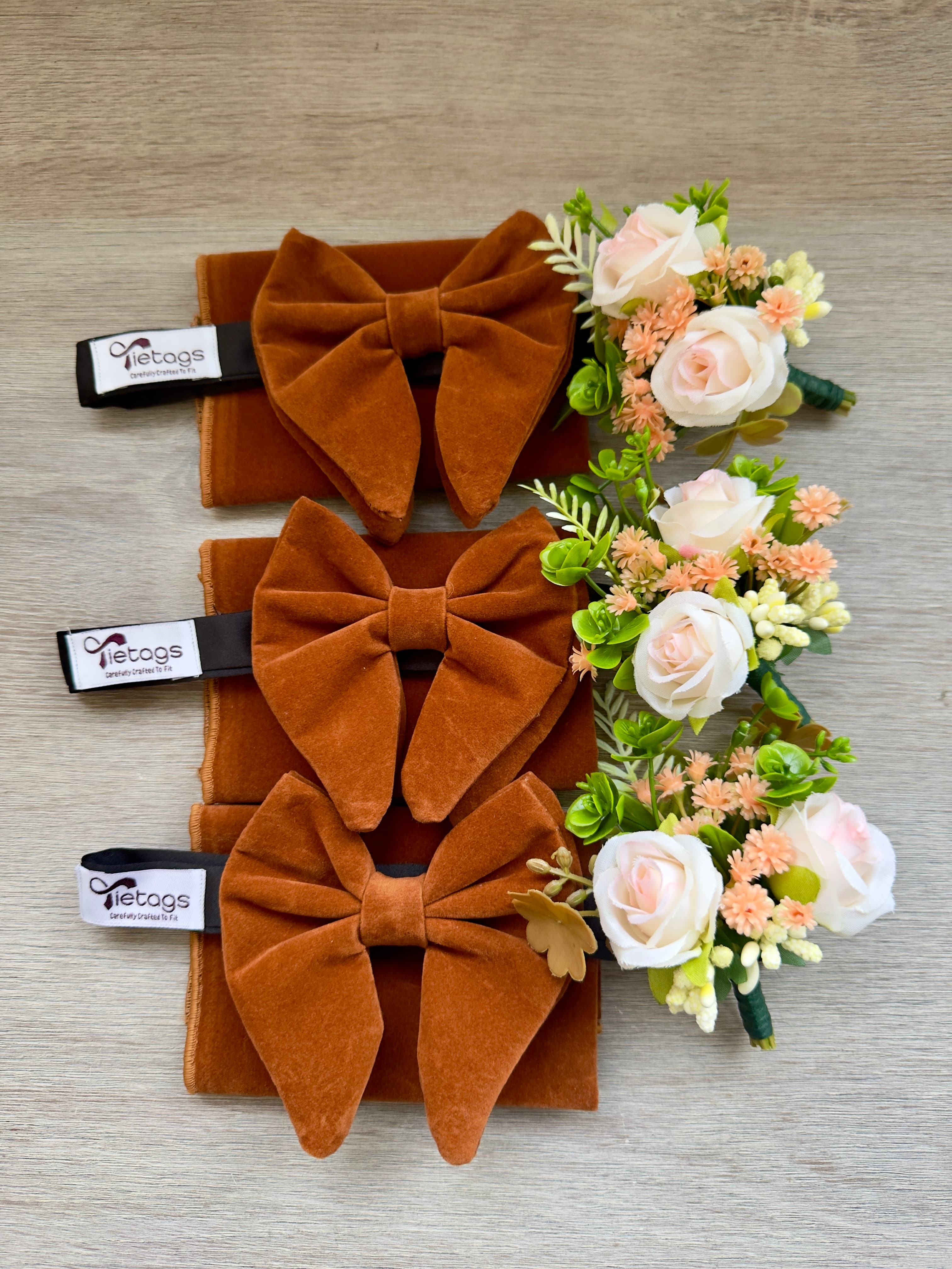 Three sets of burnt orange velvet bow ties, matching pocket squares, and floral boutonnieres.