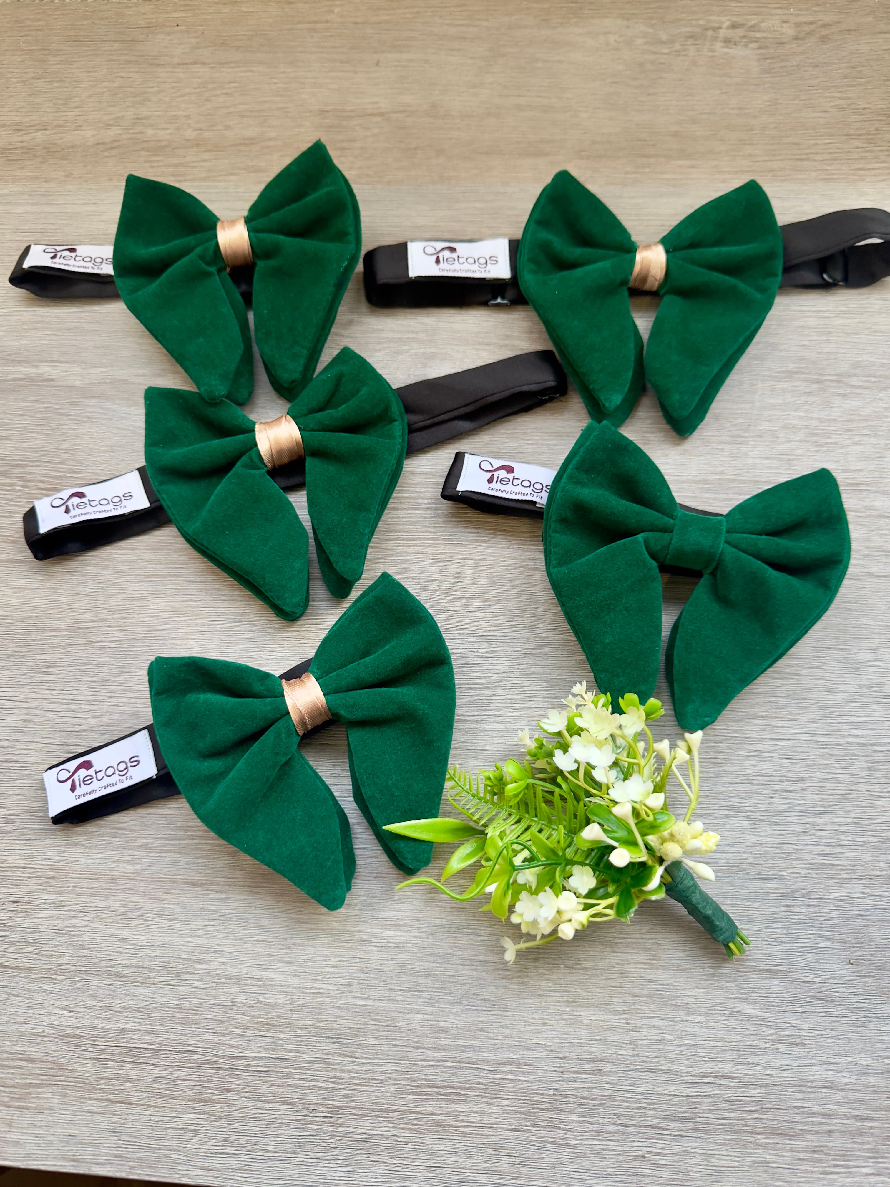 Five emerald green velvet bow ties with gold centers and a white floral boutonniere.