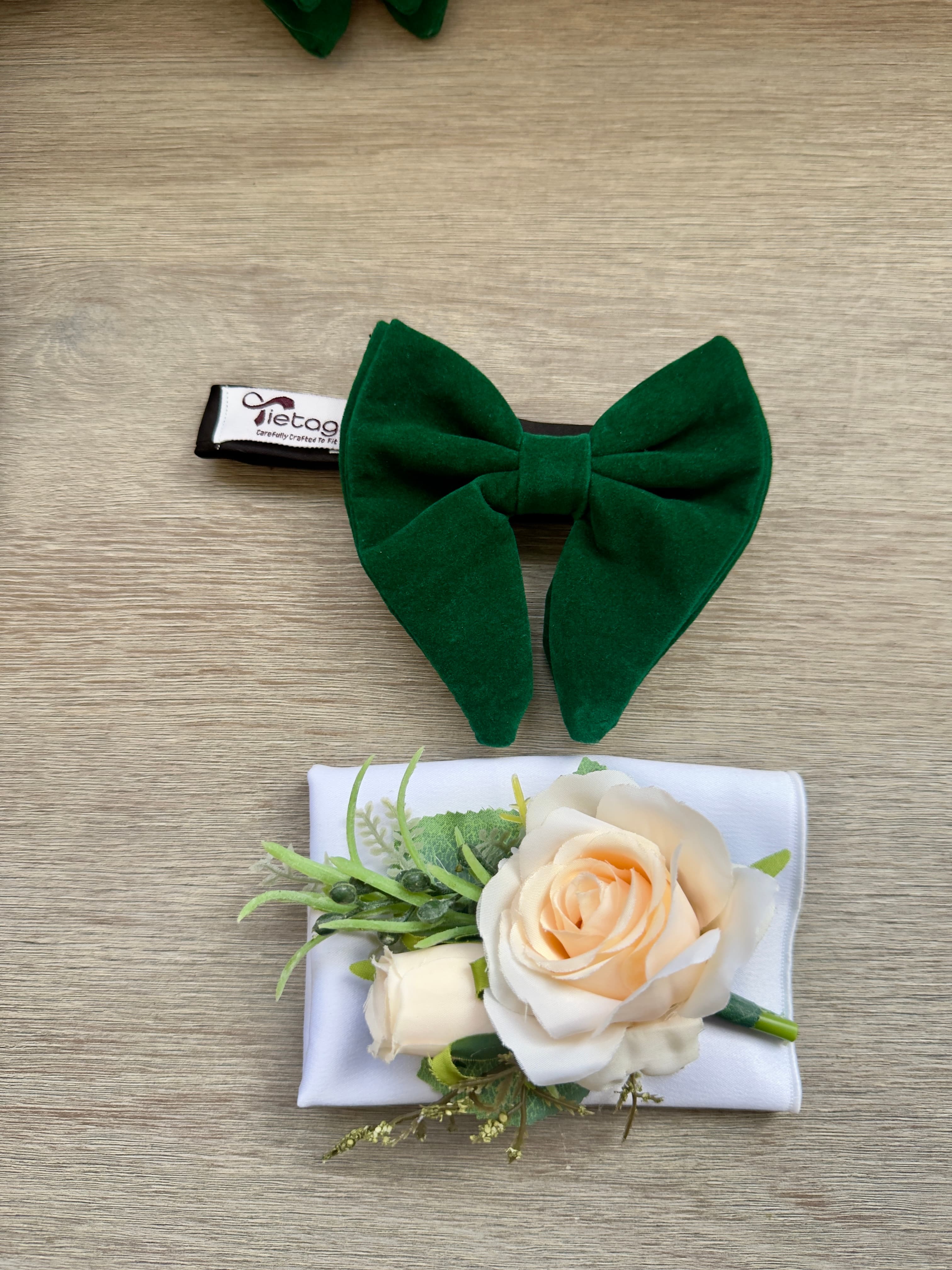 Dark green velvet bow tie and cream rose boutonniere on a white pocket square.