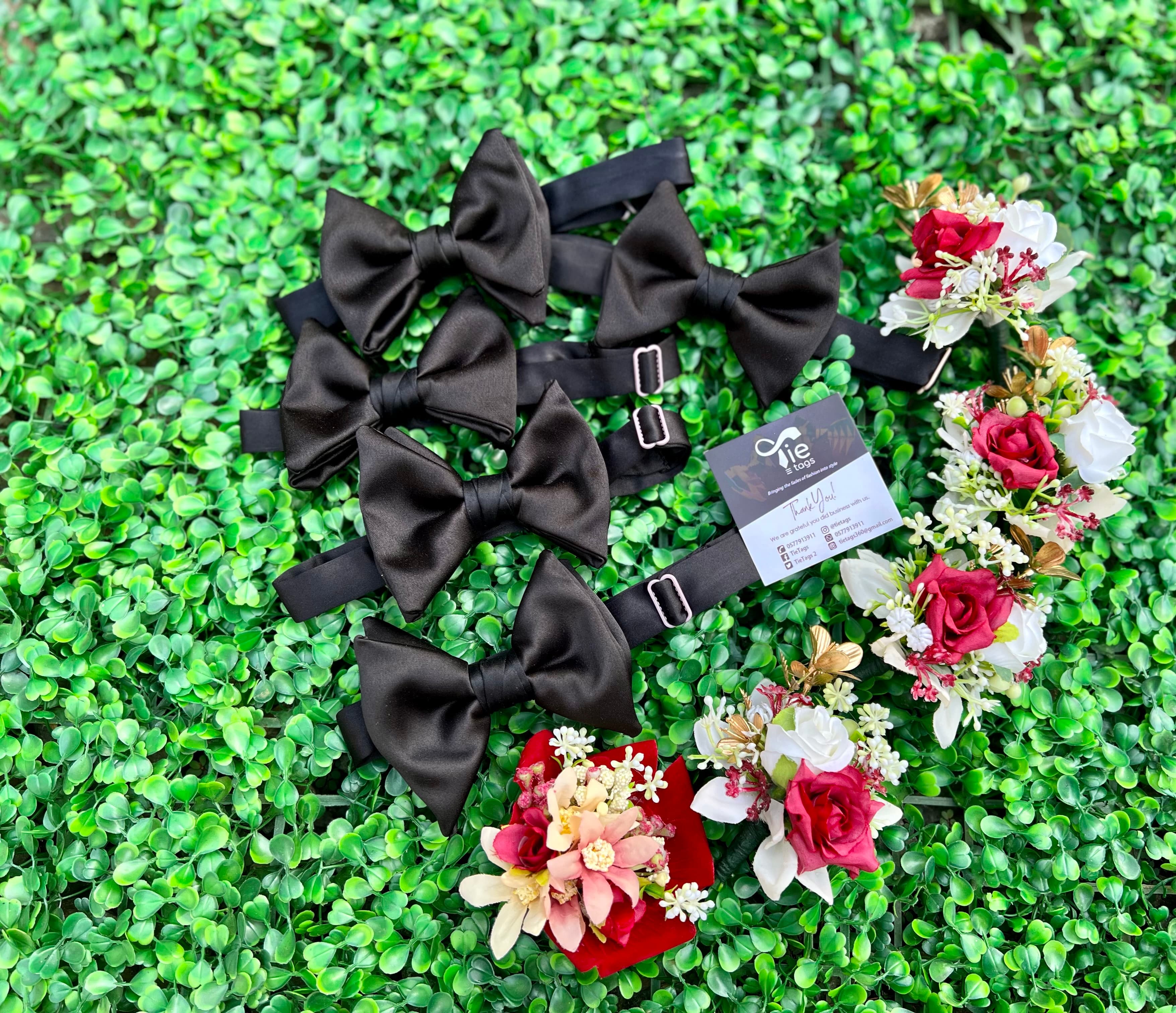 Black satin bow ties and red and white floral boutonnieres arranged on green artificial foliage.