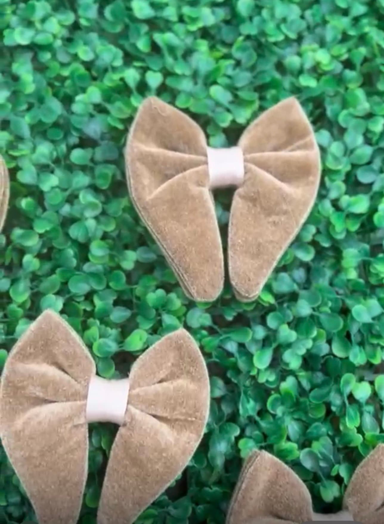 Tan velvet hair bows with cream centers displayed on a green artificial leaf background.