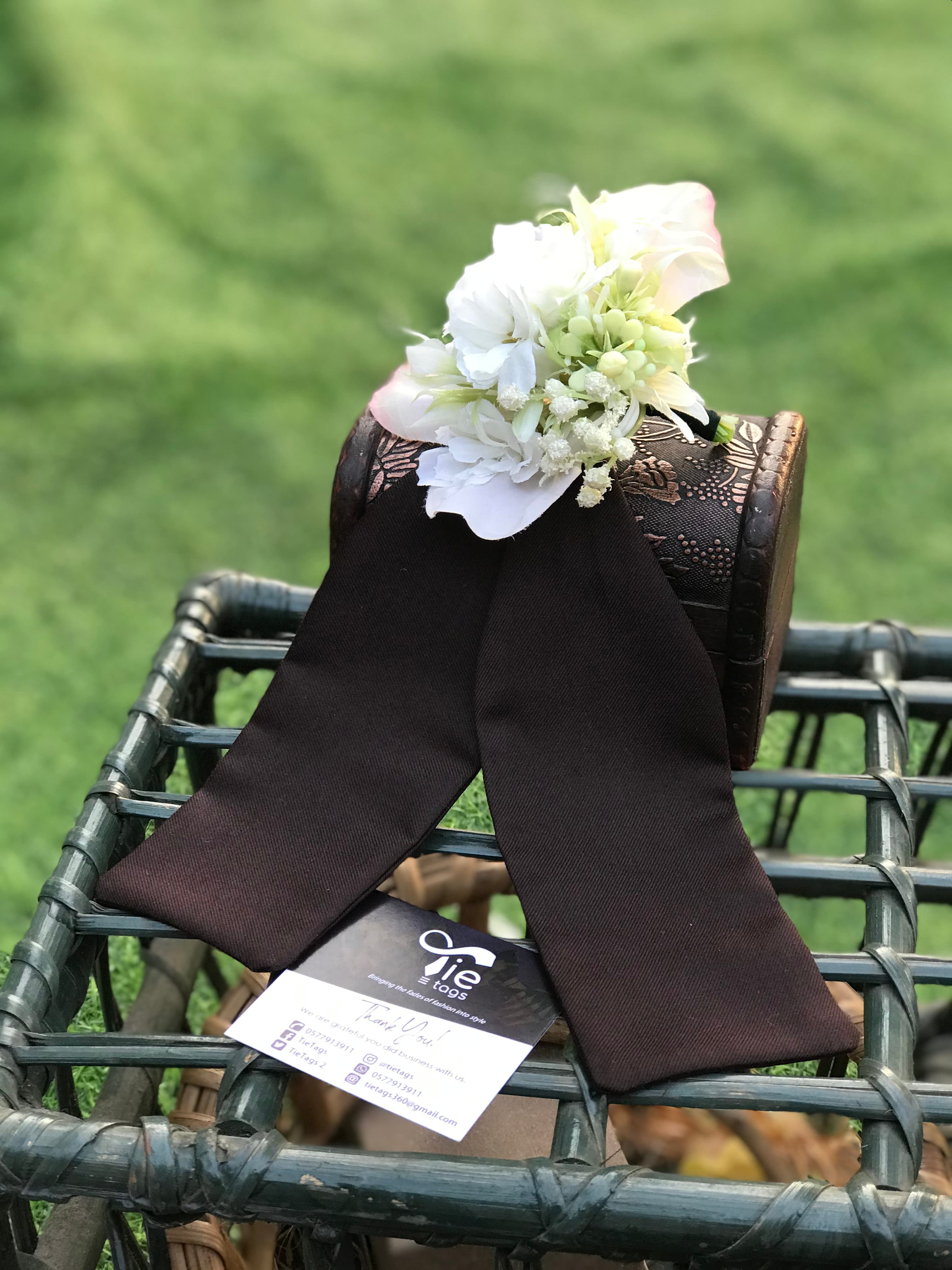 Dark brown tie and white boutonniere on an ornate chest atop a wicker basket.
